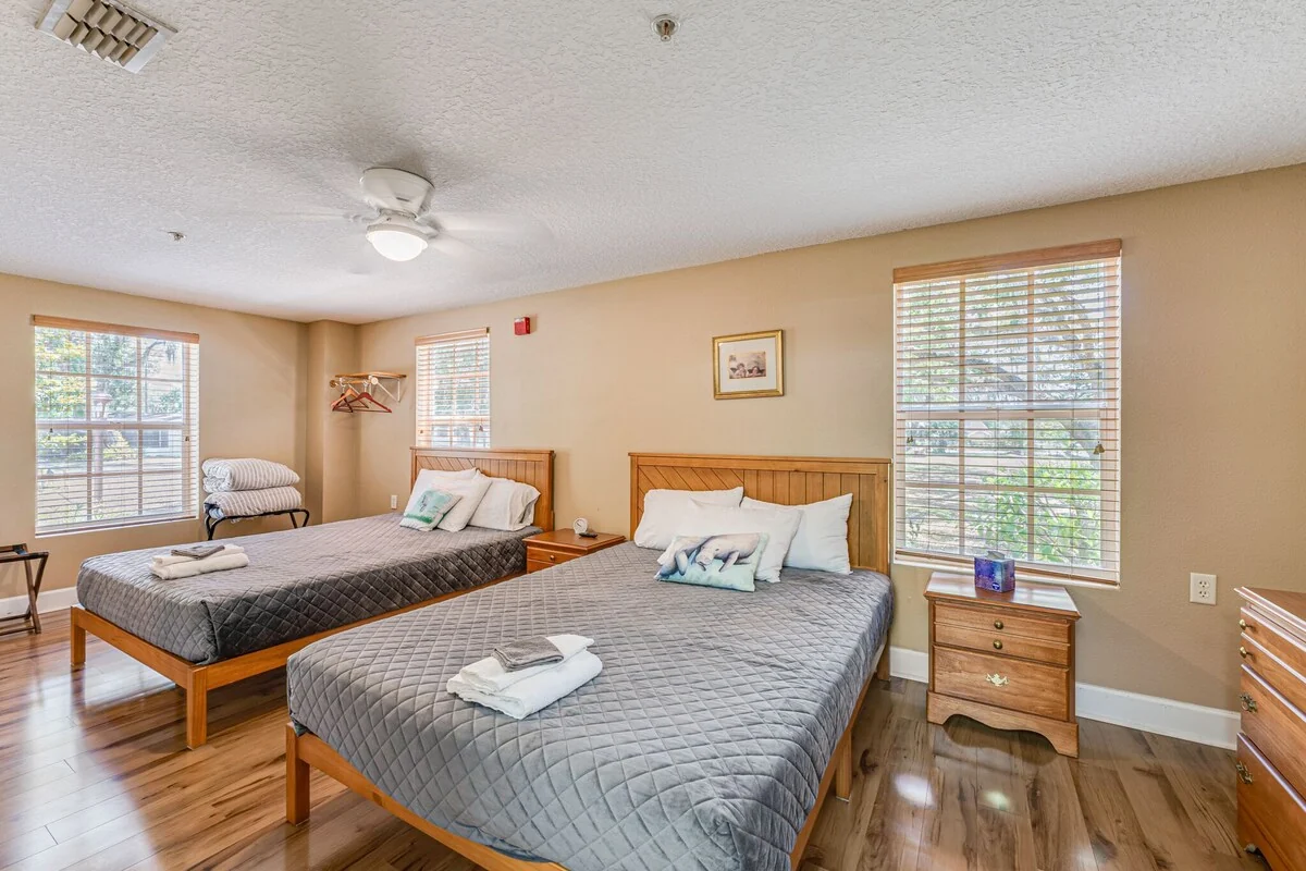 Guest room with two beds, gray quilts, wooden furniture and large windows